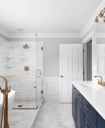 A beautiful bathroom with a blue vanity cabinet, standalone bathtub and shower, and gold faucets.